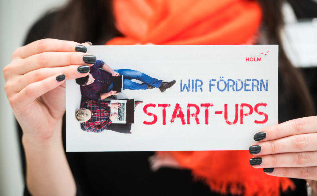 Eine Frau hält ein Schild mit der Aufschrift "Wir fördern Start-ups" in die Kamera.