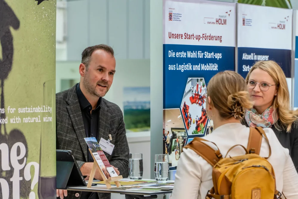 Vernetzungssituation im HOLM: 3 Personen im Gespräch. Im Hintergrund stehen Roll-ups, unter anderem von der Start-up-Förderung der HOLM GmbH.